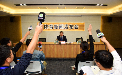 体育新闻发布厅内记者举手提问的现场画面